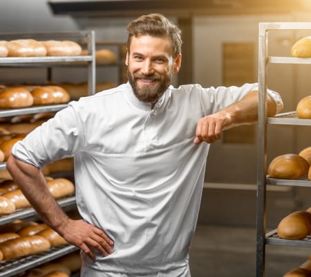 Baker standing beside racks of freshly baked bread