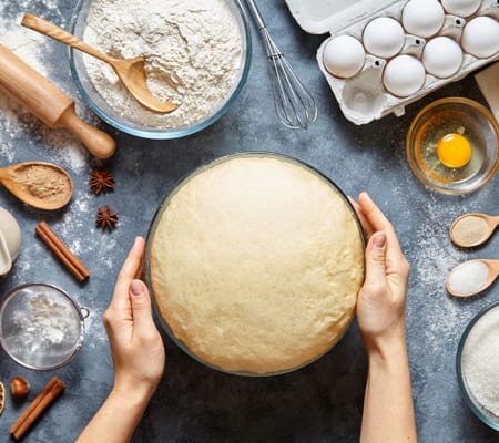 Hands kneading brioche dough beside flour, eggs and spices